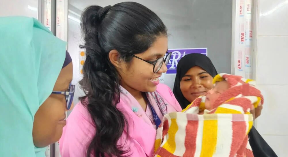 From left to right: Tamanna Jahan, Arafin Mim, and the baby’s mother gaze at a newborn they helped safely deliver. (Photo Credit: Jubayda Akter/RTM International)