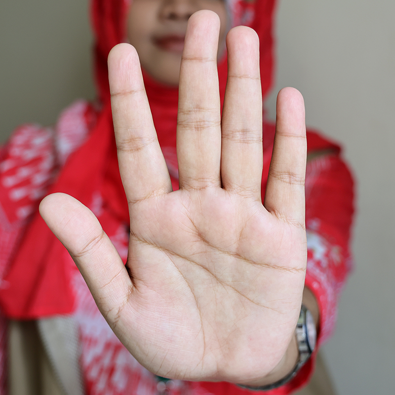 A palm of a woman's hand making a gesture to stop, covering almost the entire picture. The woman's face behind her hand is not visible.