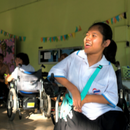 Image of a disabled girl laughing in her wheelchair as her friend, also in a wheelchair, laughs with her in the background