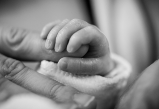 A photo of a newborn's fingers gripping the fingers of an adult
