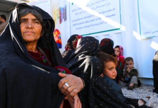 An Afghan woman, deep in thought, sits on the floor outside a UNFPA-supported mobile health clinic in Herat, Afghanistan