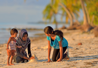 A mother and her two children play on a beach in the Maldives