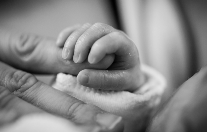 A photo of a newborn's fingers gripping the fingers of an adult
