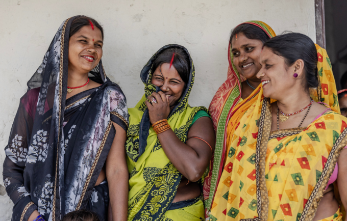 Four women in bright colours smiling and laughing. 