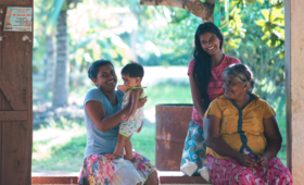 A lady with her newborn, her elder daughter, and her mother laugh while sitting outside their porch in Sri Lanka