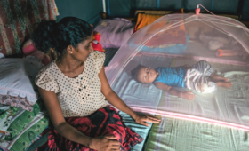 A mother looks over at her newborn as the baby lies on the bed under a mosquito net