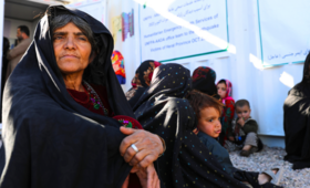 An Afghan woman, deep in thought, sits on the floor outside a UNFPA-supported mobile health clinic in Herat, Afghanistan