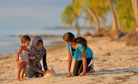 A mother and her two children play on a beach in the Maldives