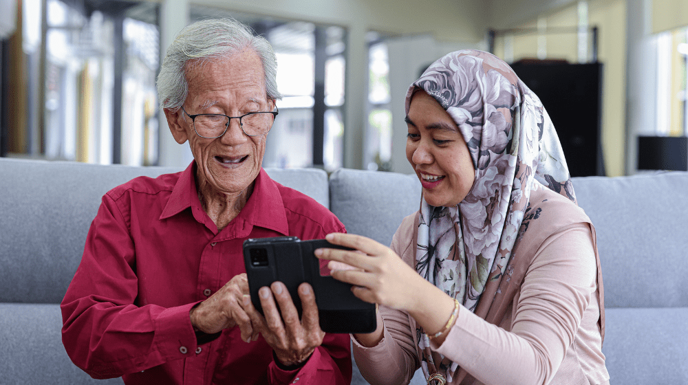 A staff at the Malaysian Research Institute on Ageing assists an elderly man to use a mobile phone for his technology-based communications (UNFPA Malaysia)