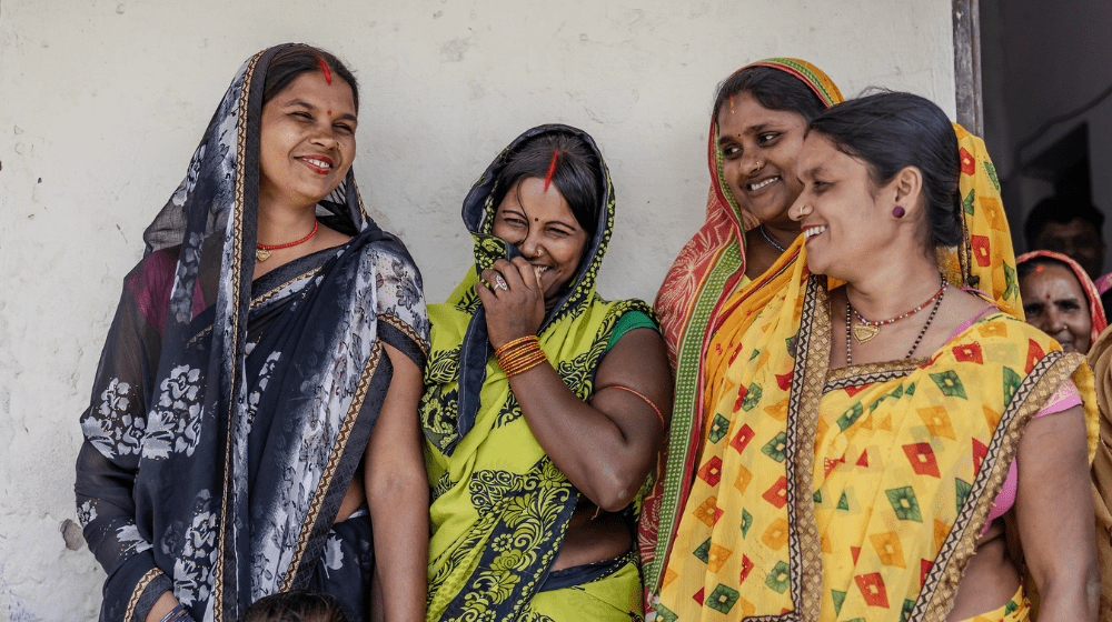 Four women in bright colours smiling and laughing. 