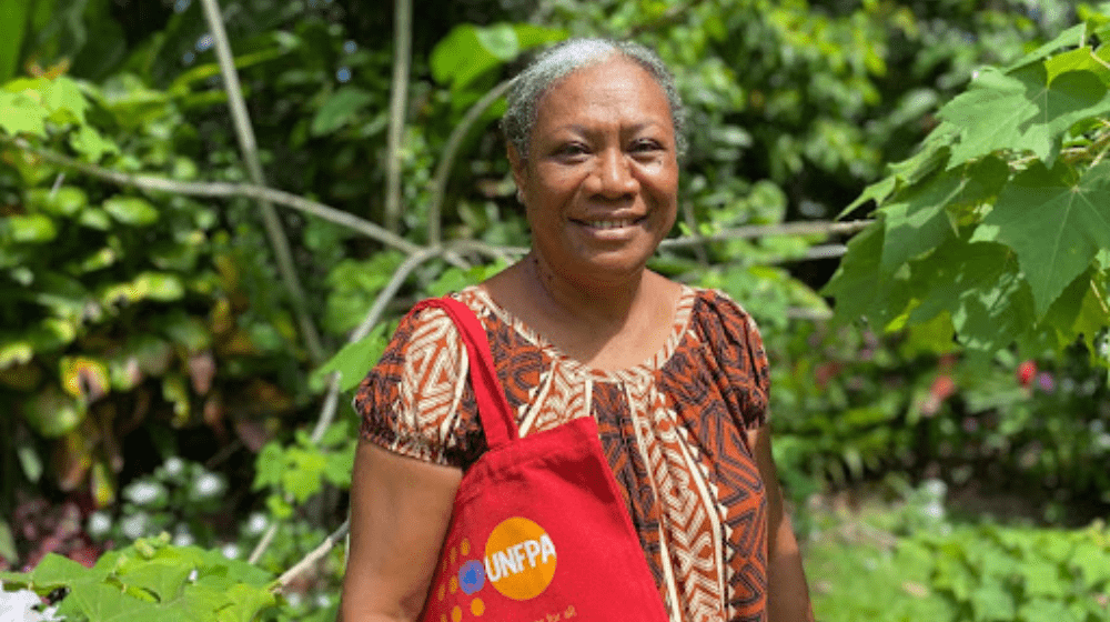Women in garden looking to camera with red UNFPA tote bag.