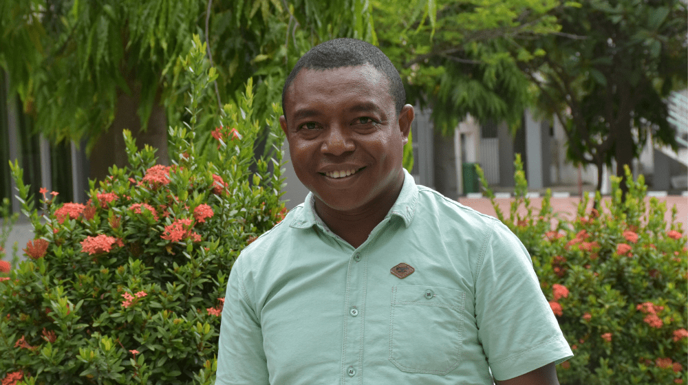 Man in green shirt looking to camera in front of garden.