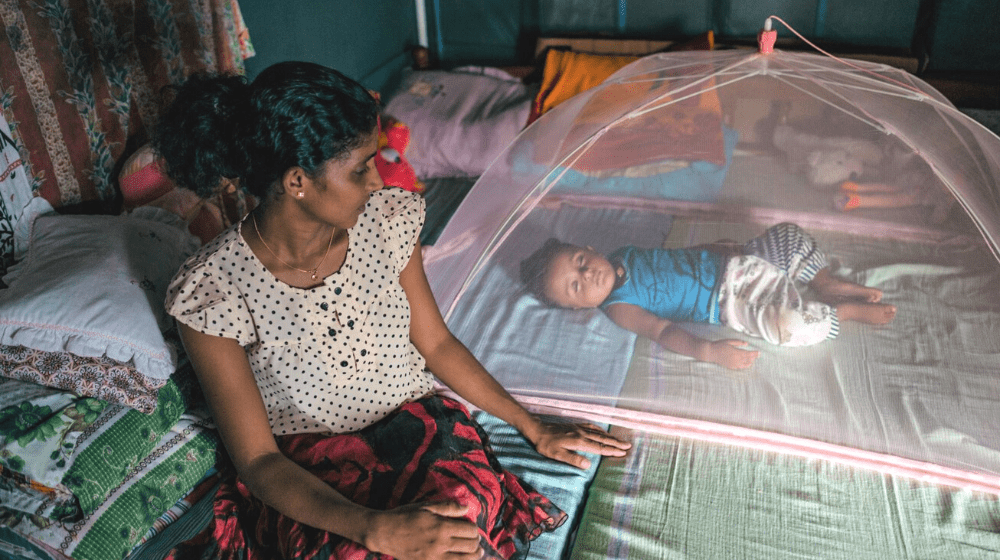 A mother looks over at her newborn as the baby lies on the bed under a mosquito net