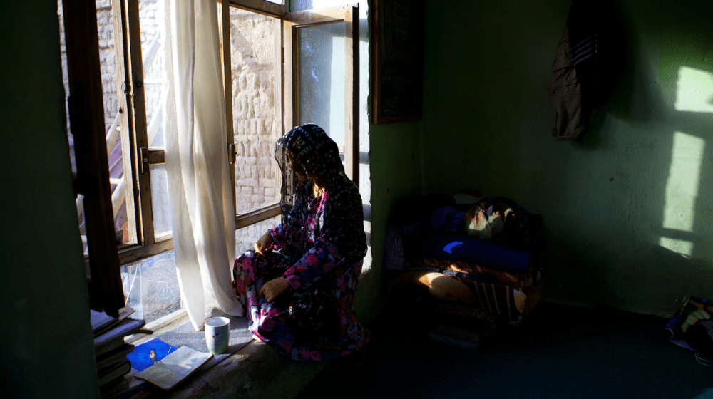 A girl sits by a window in the dark