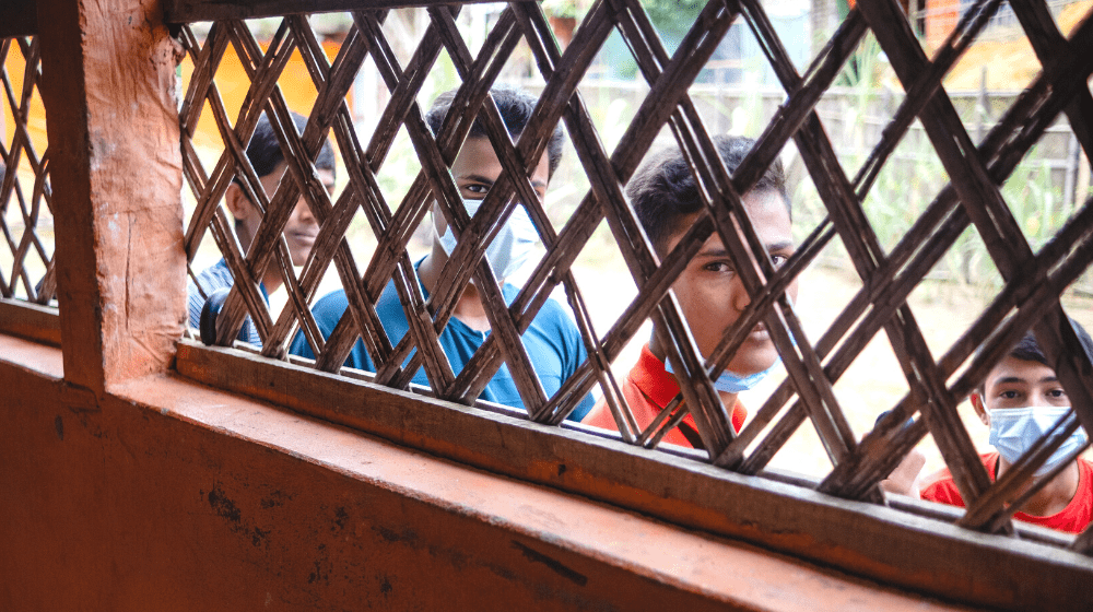 Boys living in the Rohingya camps look inside a room through the blinds