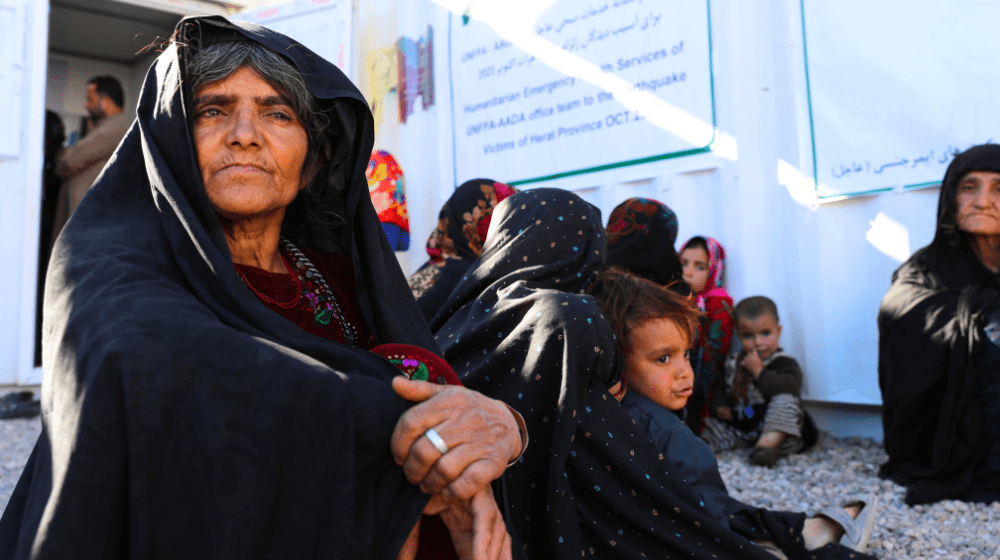 An Afghan woman, deep in thought, sits on the floor outside a UNFPA-supported mobile health clinic in Herat, Afghanistan