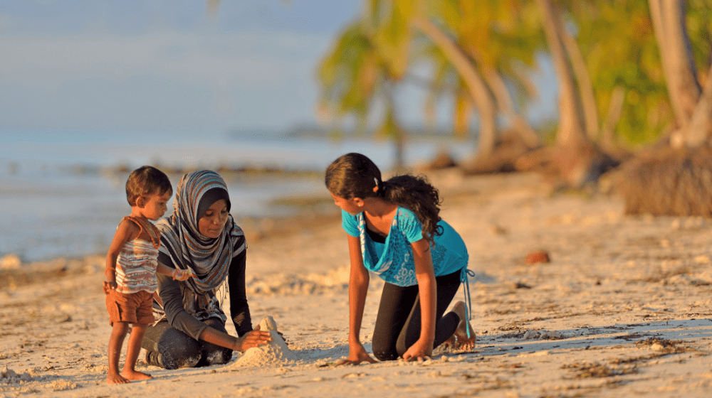 A mother and her two children play on a beach in the Maldives